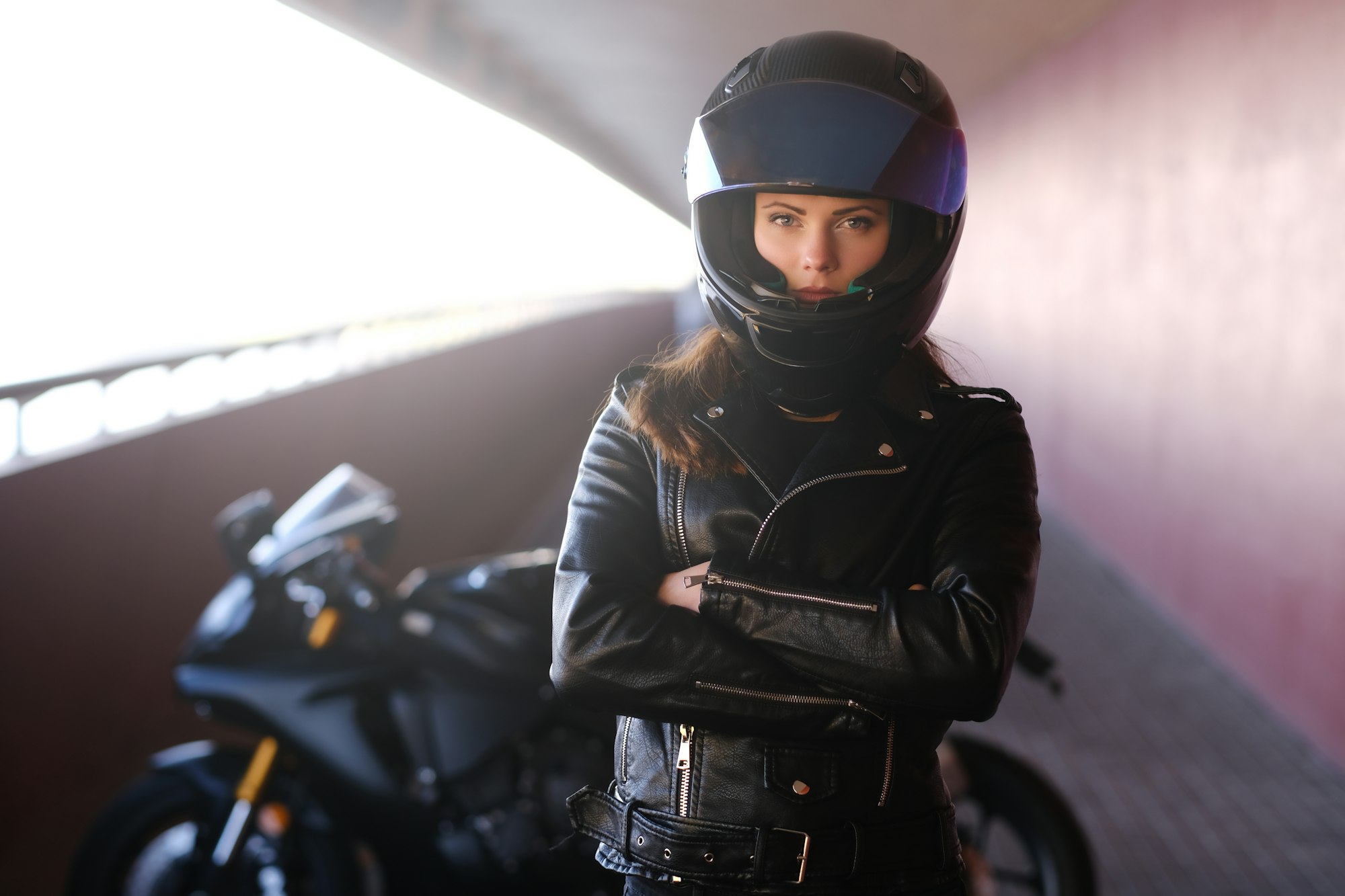 Une jolie femme sérieuse se tient à côté de sa moto en croisant les mains.