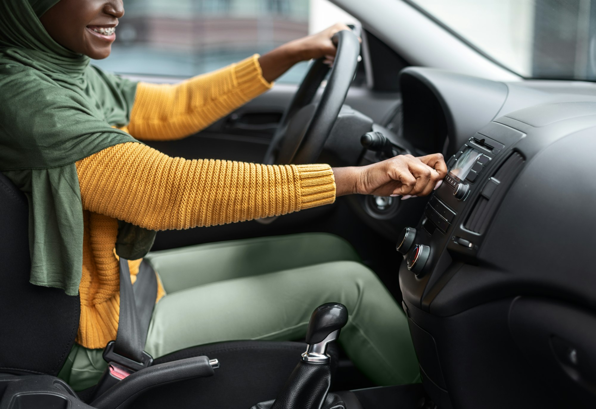 Femme musulmane noire méconnaissable allumant le volume dans le système audio de la voiture, écoutant de la musique en conduisant en ville, dame islamique africaine testant sa nouvelle automobile, image recadrée, vue latérale