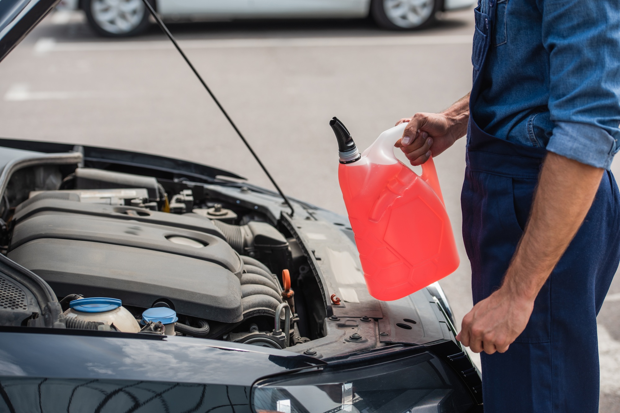 Vue courte du réparateur tenant du liquide de lave-glace à l'extérieur près de la voiture