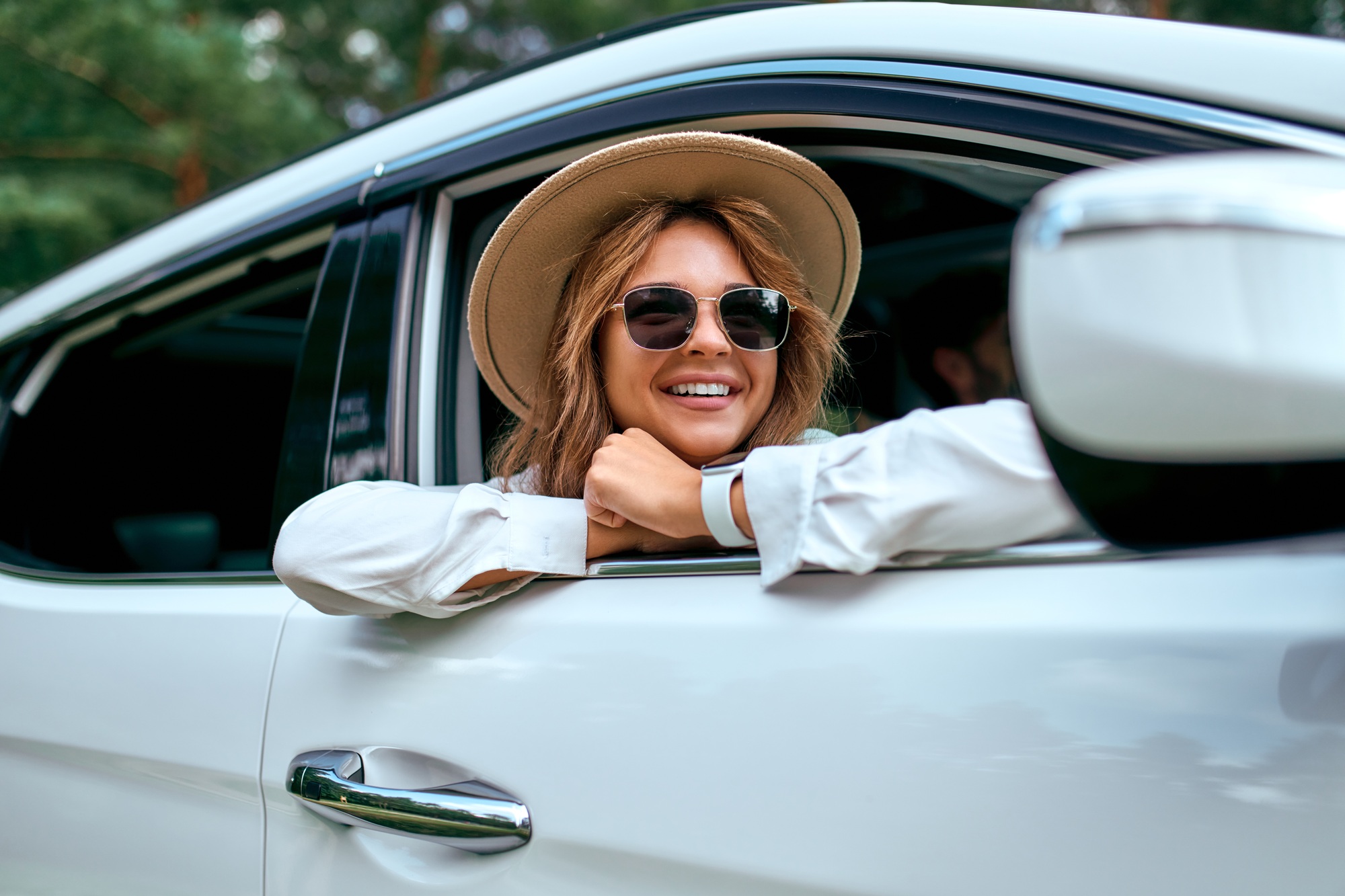 Une femme dans un chapeau et des lunettes de soleil regarde par la fenêtre de la voiture et se détend.