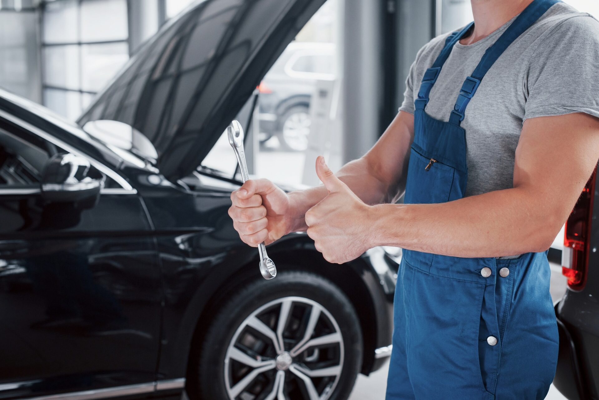 La main d'un mécanicien de voiture avec une clé dans une zone combinée près de la voiture dans l'atelier