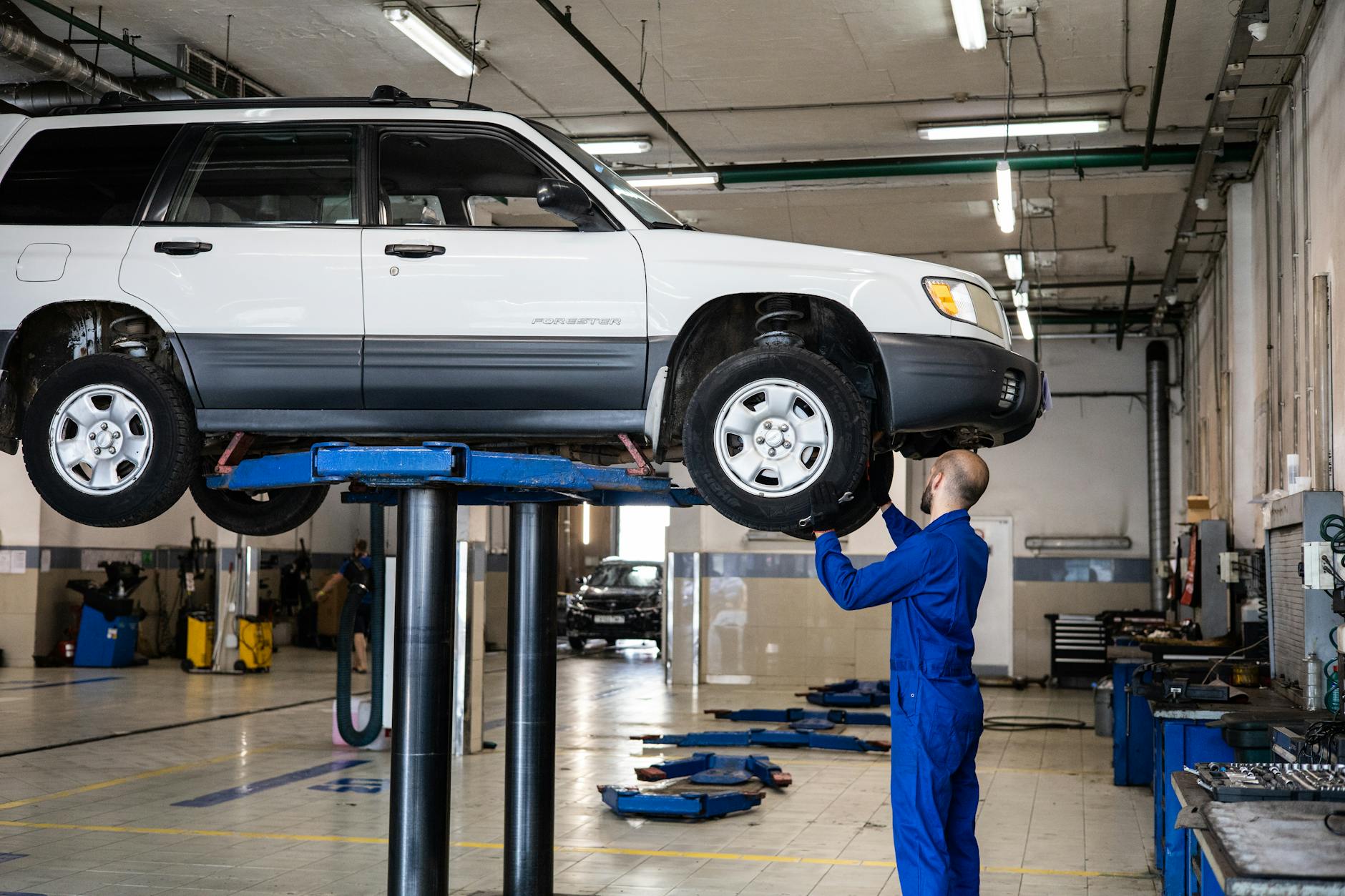Un mécanicien inspectant un SUV blanc soulevé dans un atelier de réparation automobile bien éclairé.