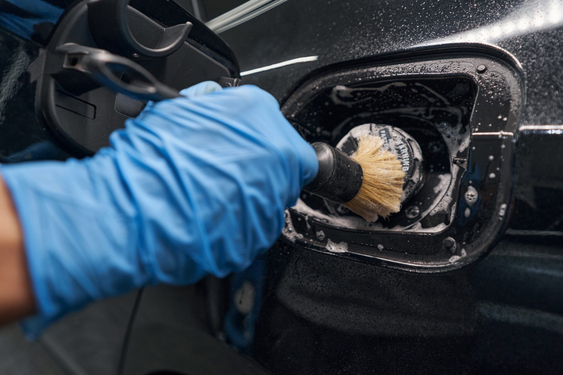 Gros plan de la main dans un gant protecteur détaillant et nettoyait soigneusement la voiture avec le détergent et le pinceau à laver