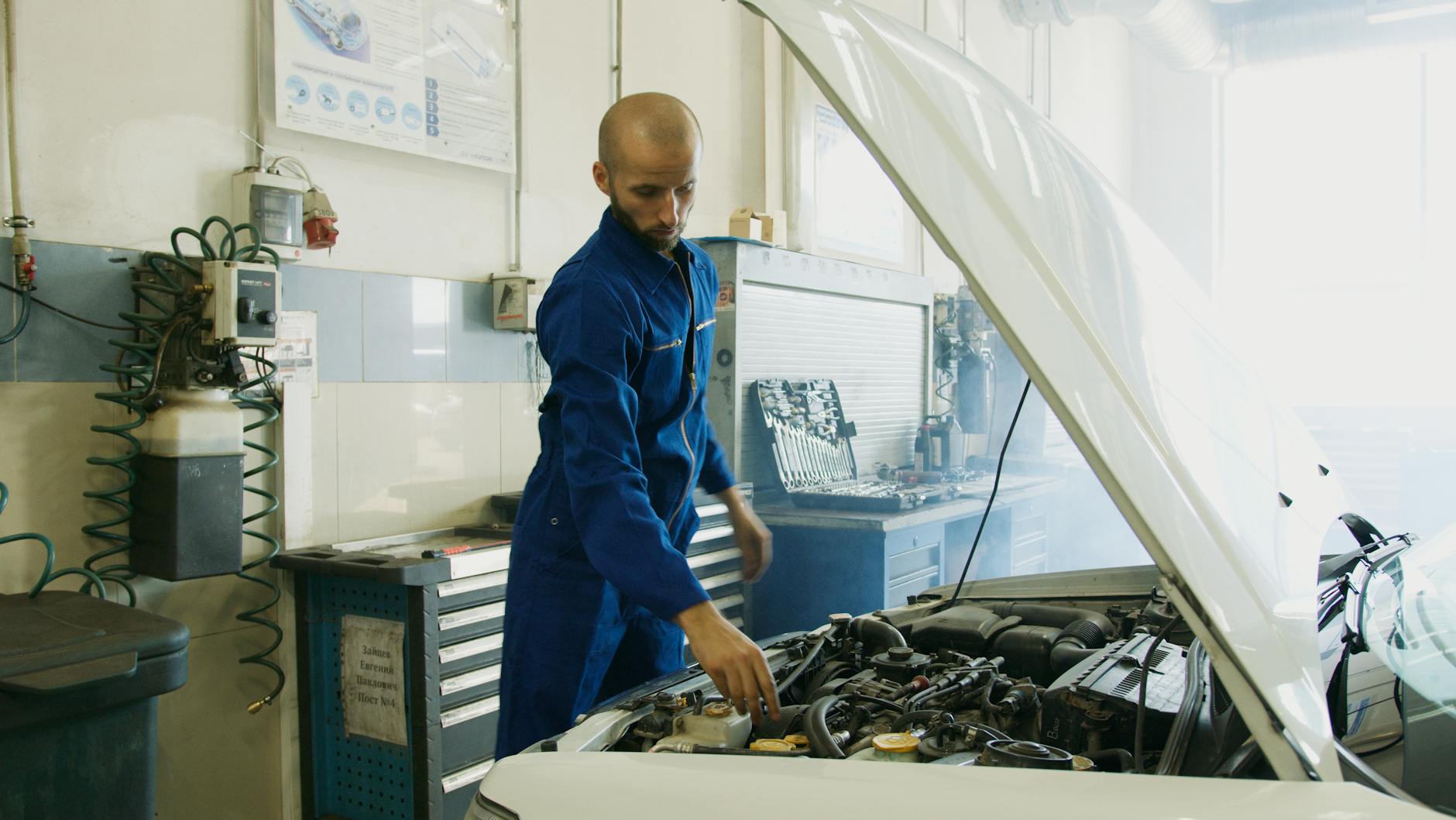 Mécanique en bleu uniforme inspectant un moteur de voiture dans un atelier.