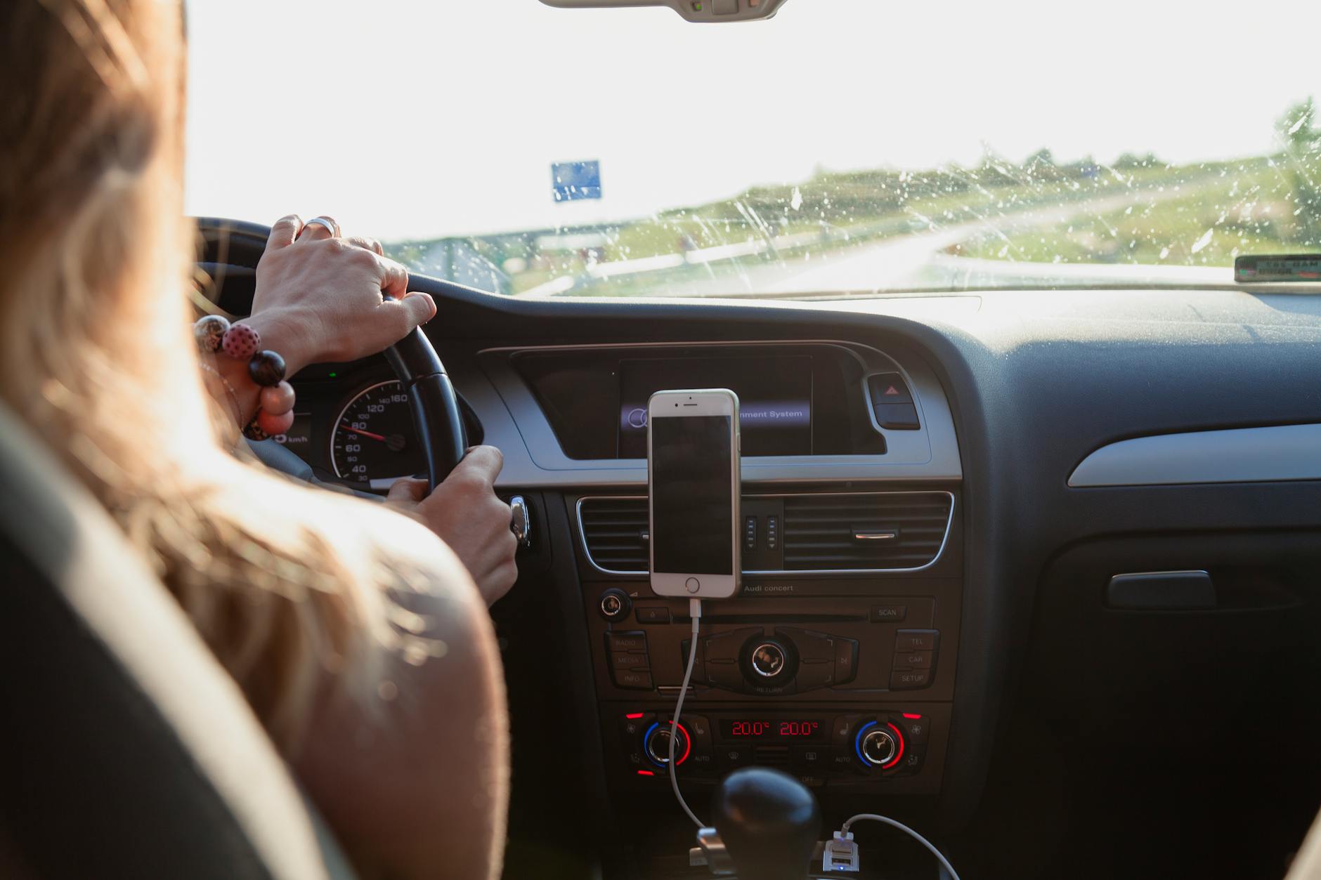 Vue de derrière une femme conduisant une voiture par une journée ensoleillée avec un téléphone monté sur le tableau de bord.