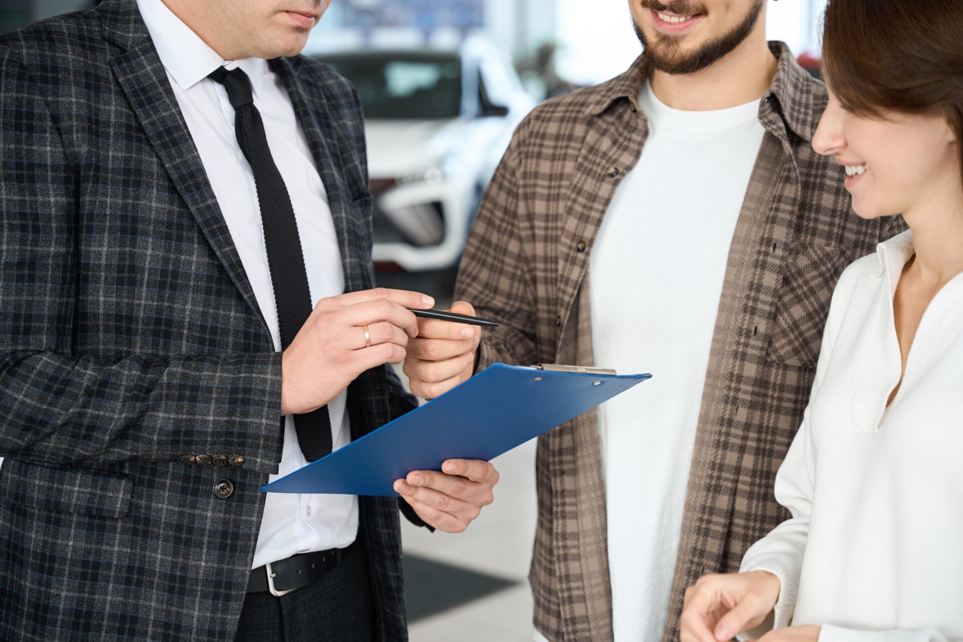 Couple méconnaissable signant certains documents avec le vendeur ou le manager achetant ou louant une voiture dans la salle d'exposition