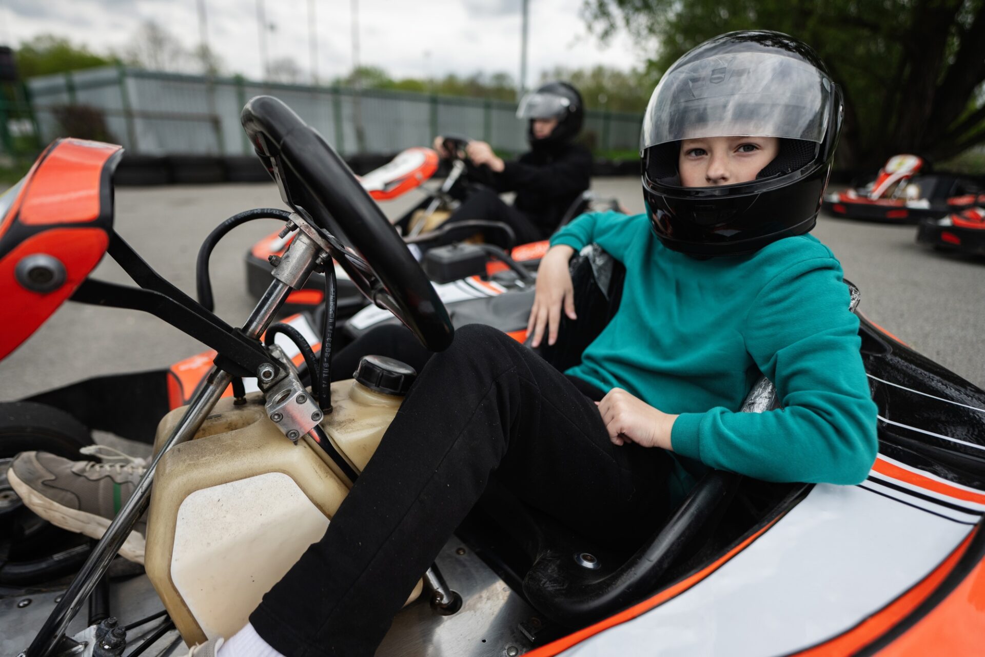 Deux enfants dans des casques qui courent des karts sur une piste en plein air, éprouvant du plaisir et de l'excitation.
