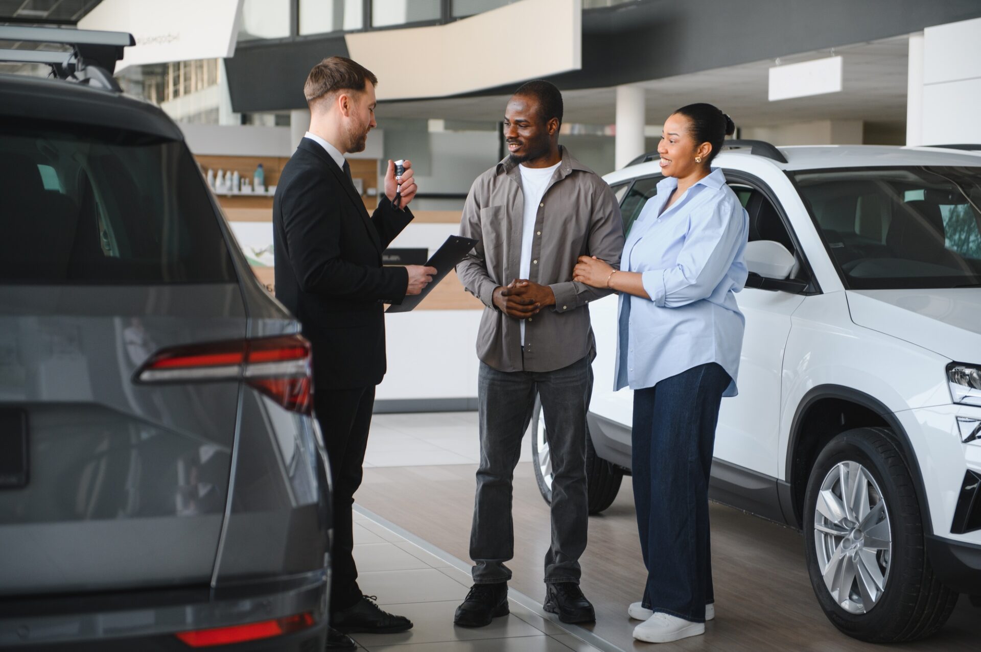 Le vendeur de voitures ait des clés de voiture et un contrat, expliquant l'accord d'achat à un couple afro-américain achetant une nouvelle voiture dans le concessionnaire