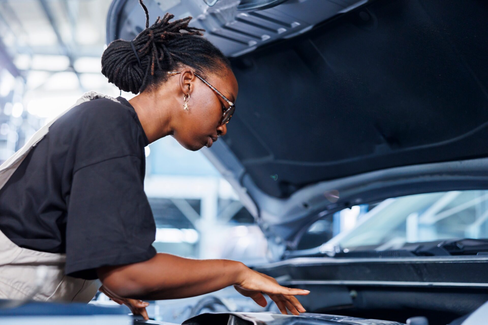 Bipoc Woman en service automobile utilisant un outil mécanique professionnel pour réparer le système d'allumage cassé.