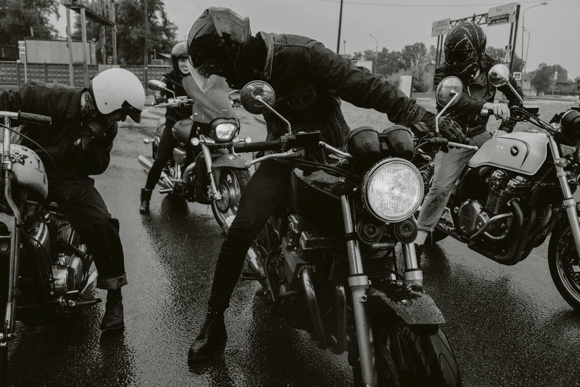 Groupe de motocyclistes roulant dans une rue humide présentant une ambiance dynamique et aventureuse.