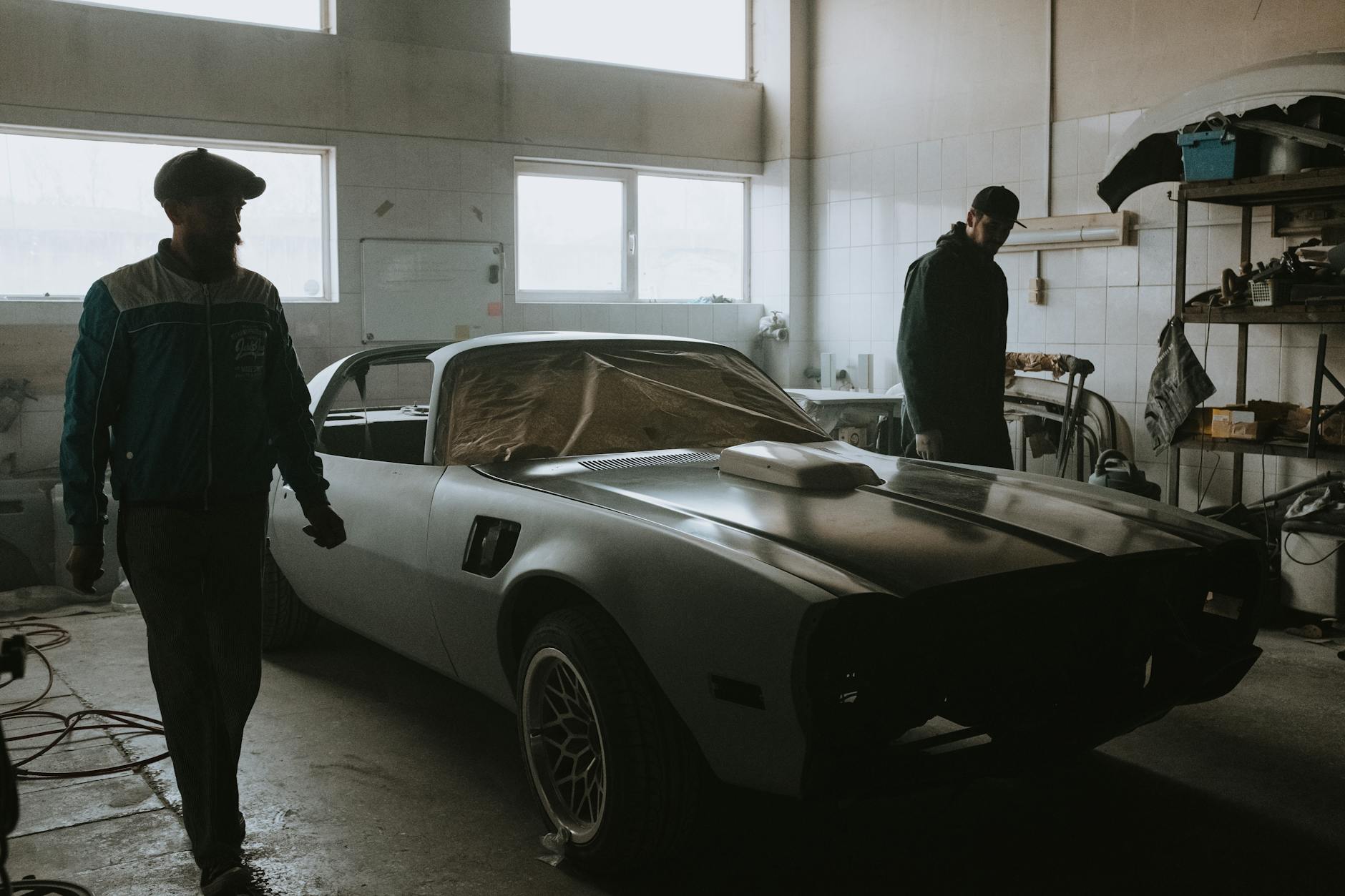 Mécanique travaillant sur une restauration de voitures vintage dans un garage faiblement éclairé, capturant l'essence des soins automobiles classiques.