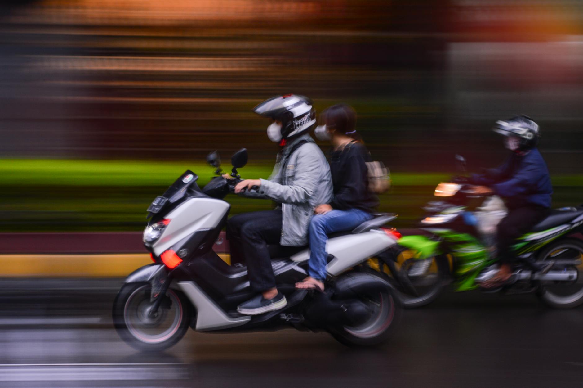 Capture de mouvements flous de personnes en scooter se précipitant dans les rues de la ville, évoquant la mobilité urbaine.