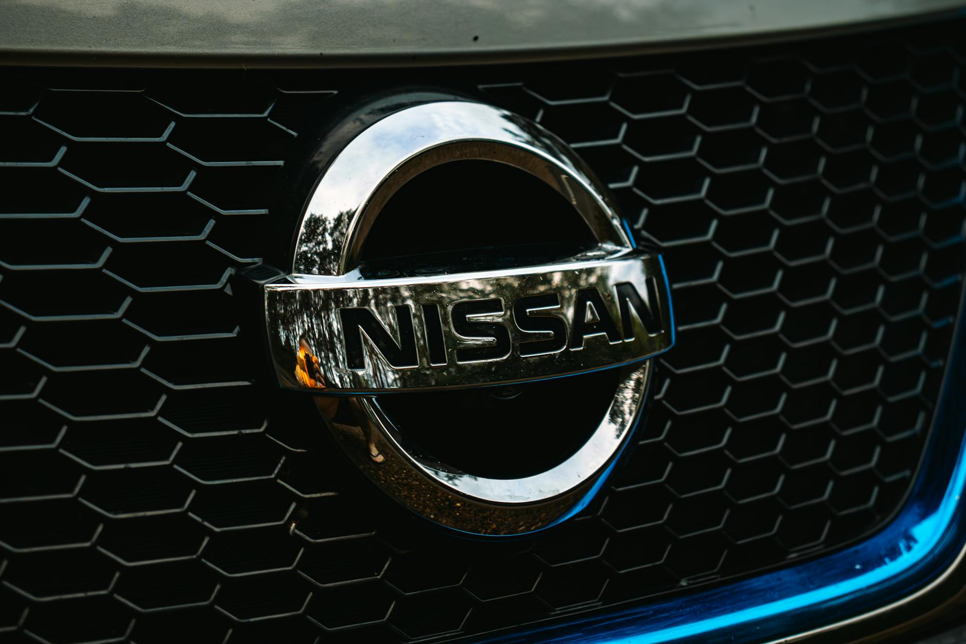 Prise de vue détaillée du logo Nissan sur une grille de calandre de voiture, mettant l'accent sur l'image de marque automobile.