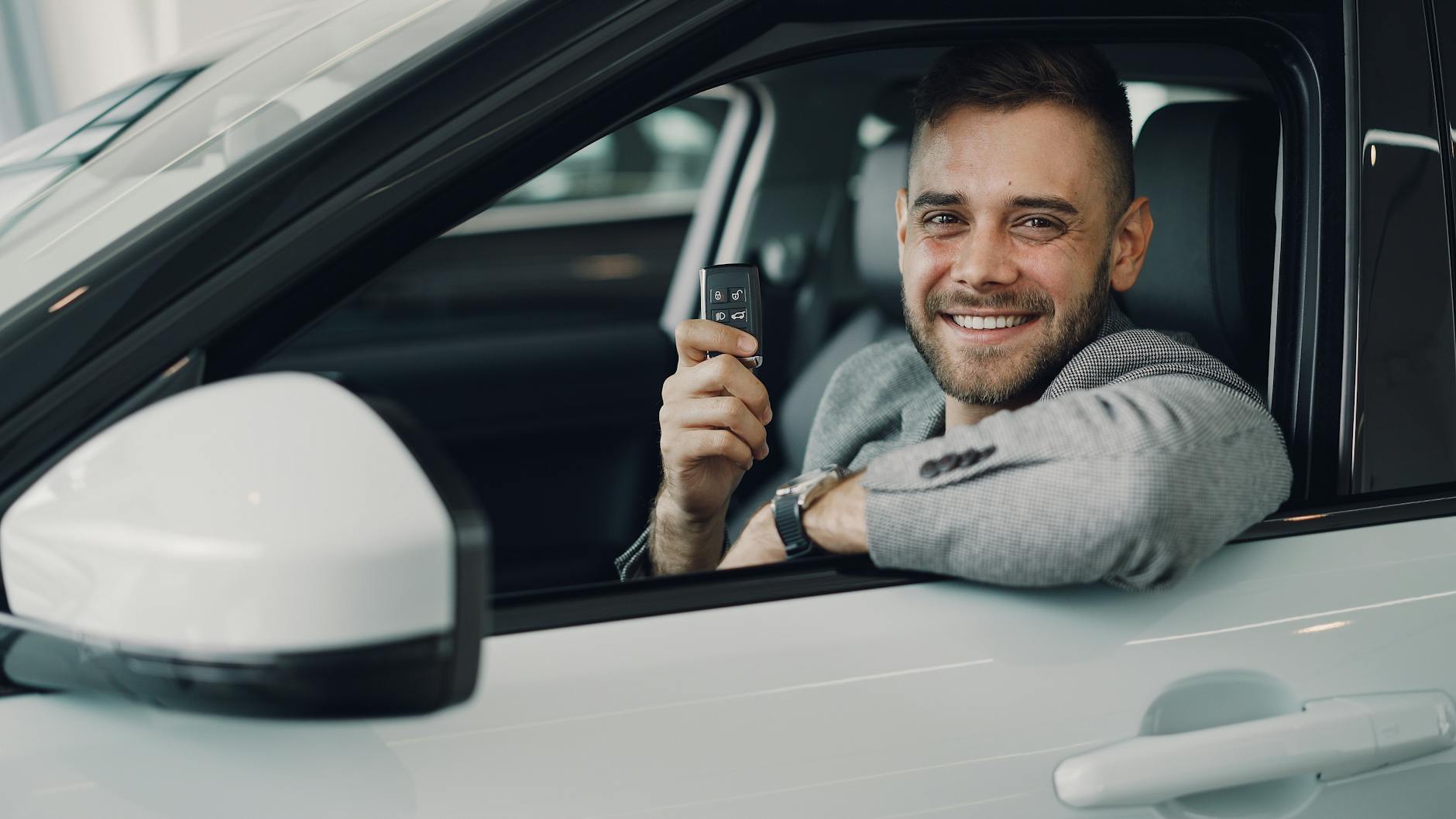 Heureux jeune homme tenant les clés de voiture à l'intérieur d'un véhicule.