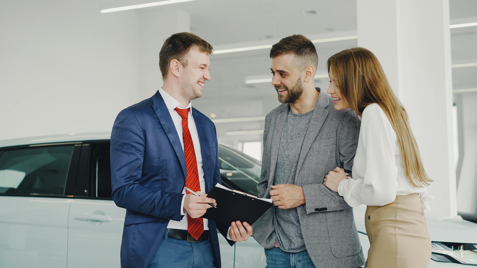 Un couple souriant achète une nouvelle voiture à un vendeur confiant dans un concessionnaire automobile moderne.