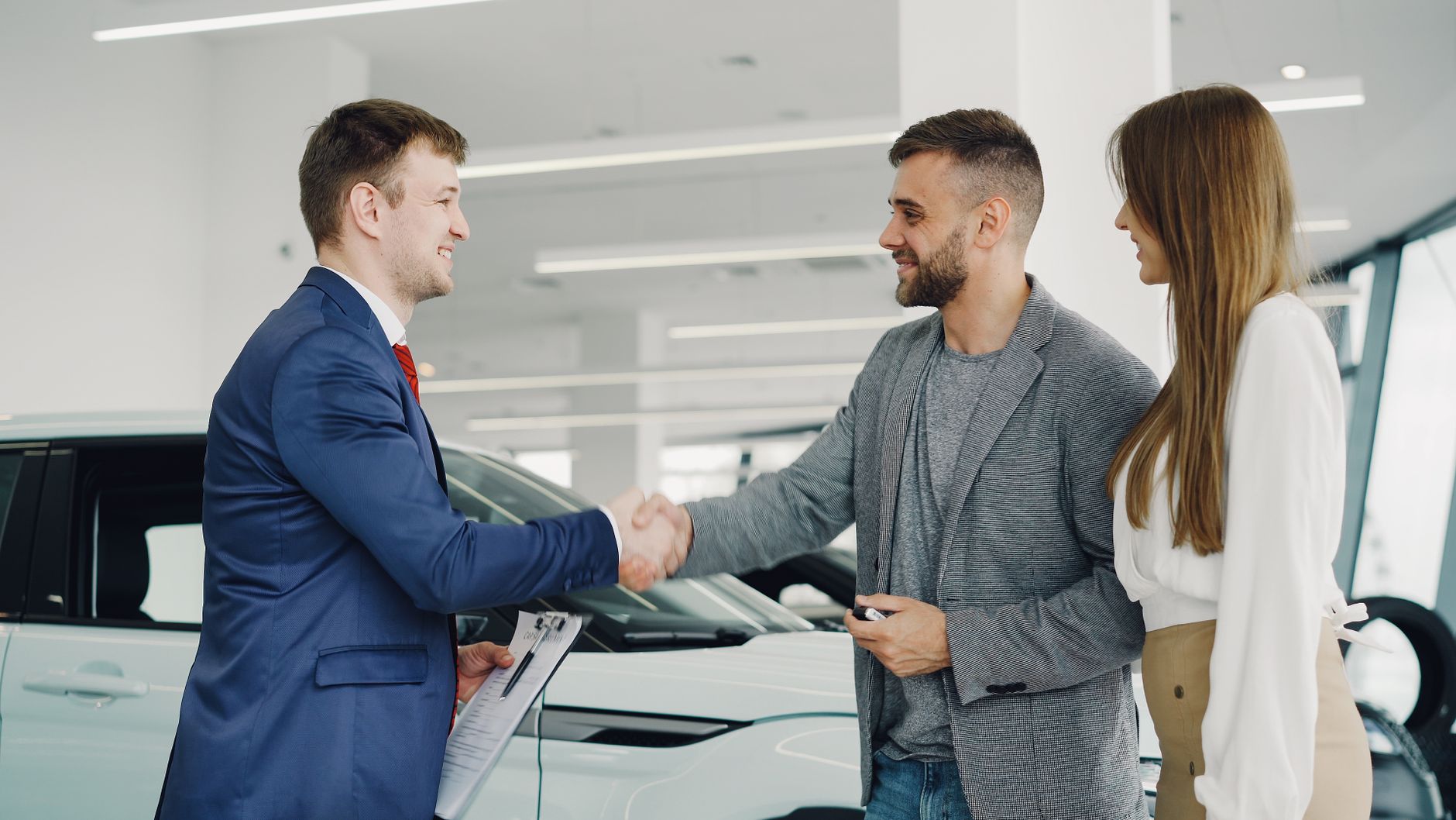 Poignée de main amicale entre un vendeur de voitures et des clients dans une salle d'exposition automobile moderne.