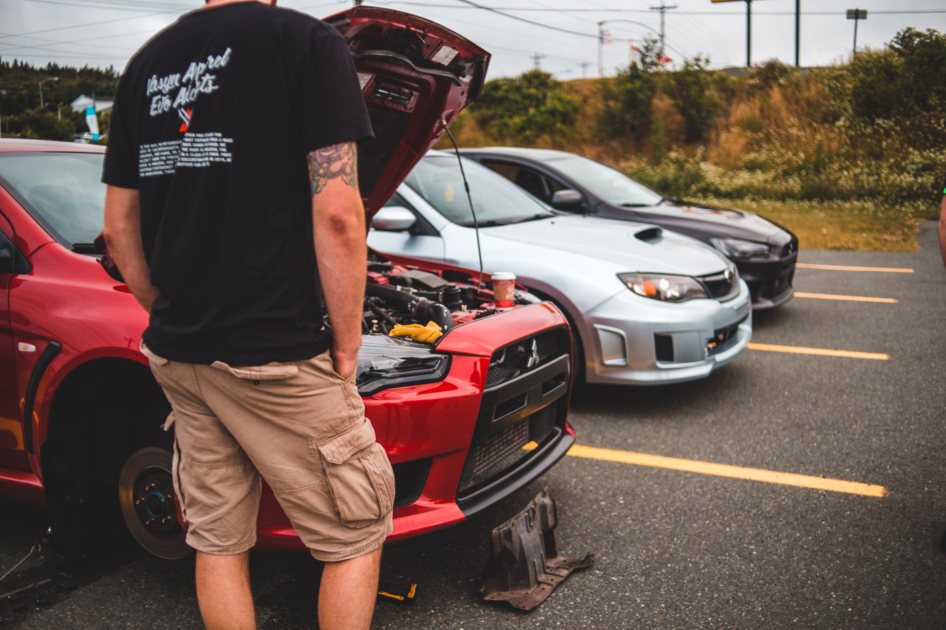 Un homme inspecte le capot ouvert d'une voiture de sport modifiée lors d'une rencontre automobile en plein air.