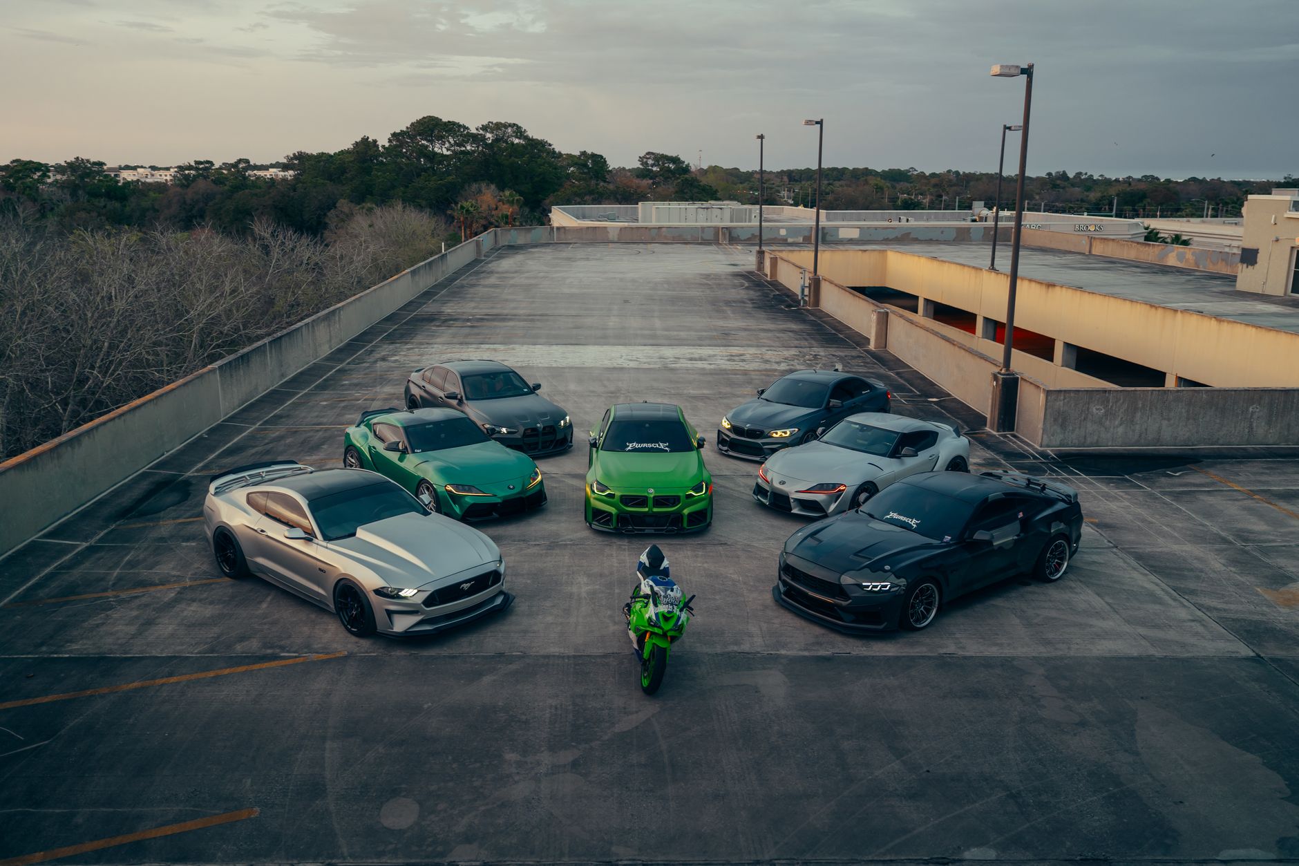 Une collection de voitures haut de gamme et une moto sur un parking sur le toit au crépuscule, mettant en valeur l'élégance automobile.