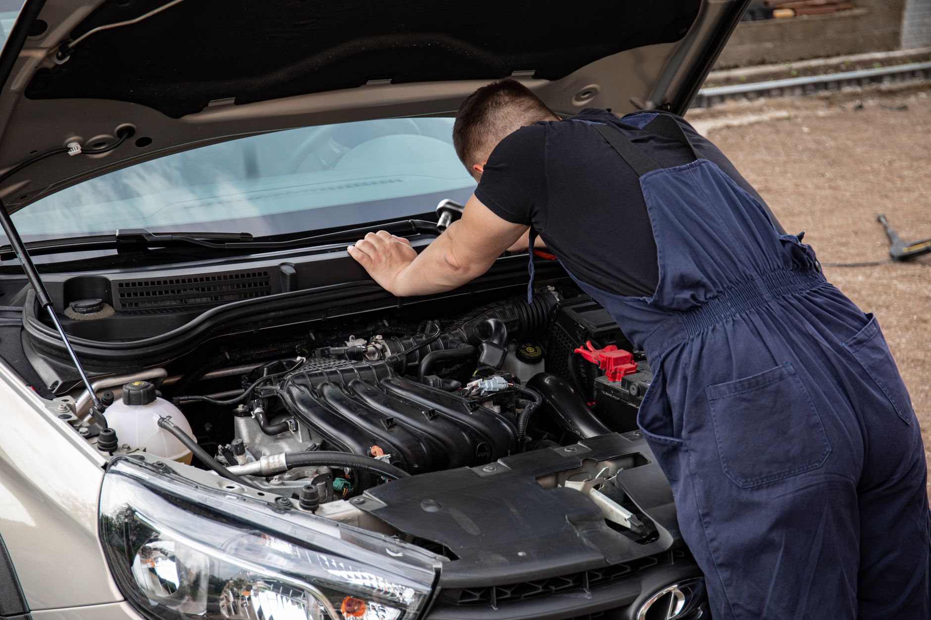 Un mécanicien vérifie le moteur d'une voiture à l'extérieur, se concentrant sur l'entretien et la réparation du véhicule.
