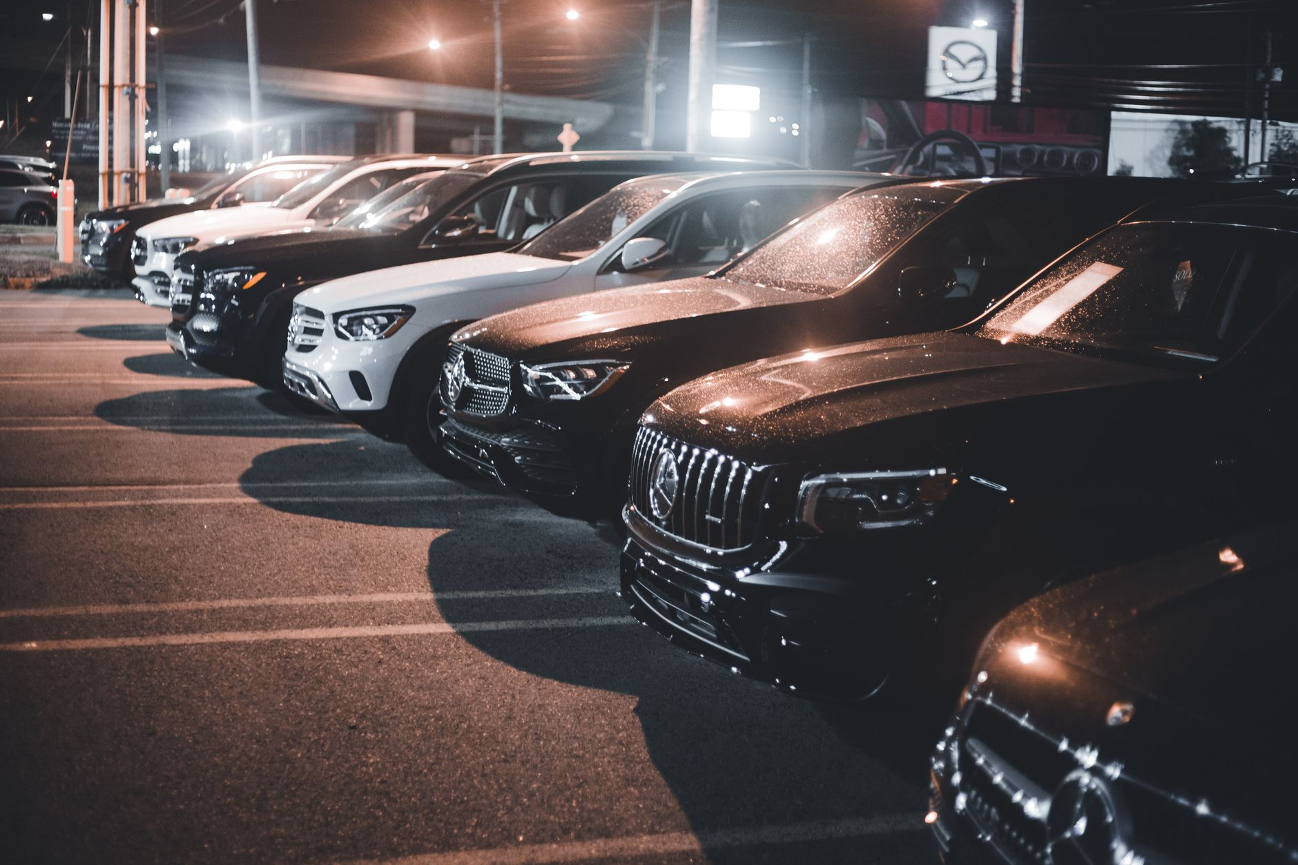 Rangée de voitures de luxe sur un parking la nuit, illuminées par les lampadaires.